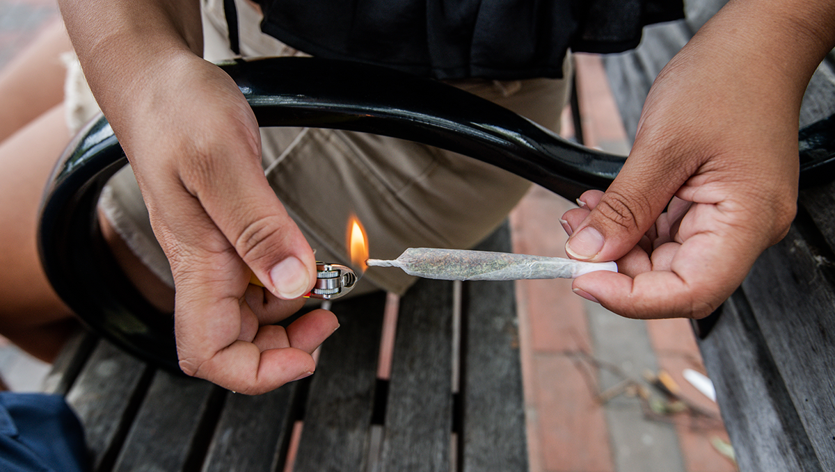 More Liberal Cannabis Laws Lead to Fewer Spice/K2 Overdoses: A woman's hands as she lights up a cannabis joint sitting on a park bench More Liberal Cannabis Laws Lead to Fewer Spice/K2 Overdoses: A woman's hands as she lights up a cannabis joint sitting on a park bench