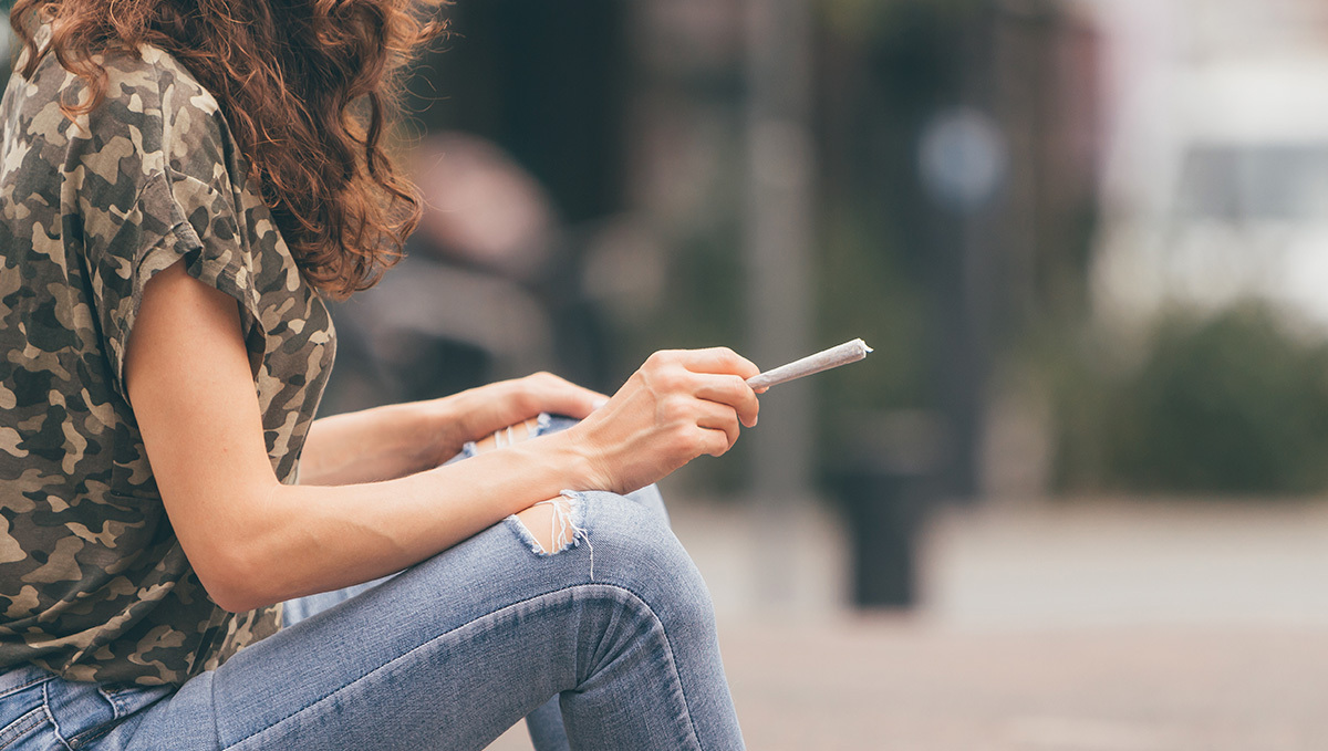 Spain to Legalize Medical Cannabis Sales This Year: A young woman in denim an khaki shirt sitting on a curb with an unlit joint in hand Spain to Legalize Medical Cannabis Sales This Year: A young woman in denim an khaki shirt sitting on a curb with an unlit joint in hand
