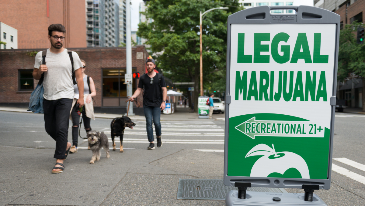 People walking their dogs and looking at a legal-marijuana sign