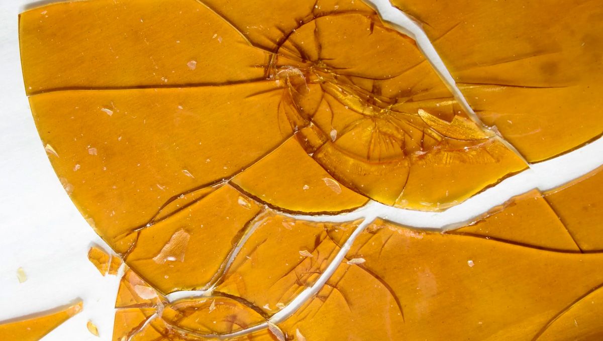 Cannabis Shatter: What Is It, How To Make And Smoke THC & CBD Hash Oil: A sheet of shatter lying on a white surface and broken into several pieces